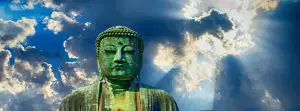 Een groot boeddhabeeld met daarachter de zon die door de wolken breekt